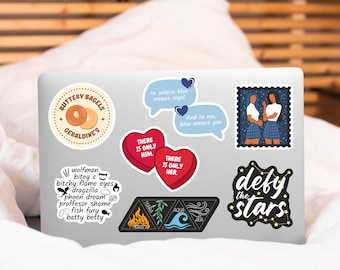 May include: A silver laptop with various stickers, including a heart with the text "There is only him", a heart with the text "There is only her", a sticker with the text "Buttery Bagels Geraldine's", a sticker with the text "In solaria blue means royal", a sticker with the text "And to me, blue means you", a sticker with the text "Defy the stars", a sticker with the text "wolfman bitey c bitchy flame eyes dragzilla phoen dream proffesor shame fish fury batty betty", and a sticker with four triangles, each with a different element: fire, earth, water, and air.