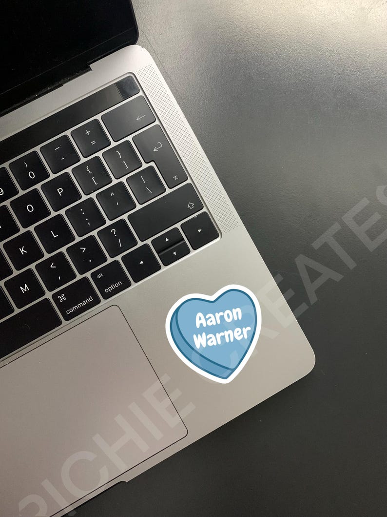 May include: A blue heart-shaped sticker with the text "Aaron Warner" on a silver laptop.