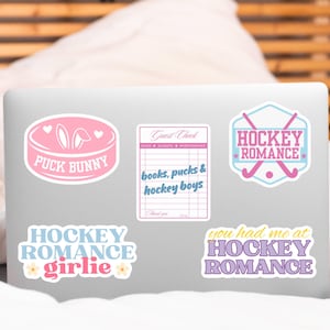 May include: A collection of stickers with hockey-themed designs. The stickers feature phrases like "Puck Bunny," "Hockey Romance," and "Hockey Girlie." The color palette includes pink, blue, and purple.