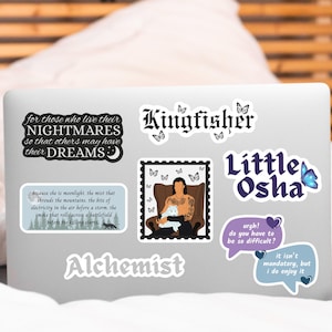 May include: A collection of stickers on a laptop. The stickers feature various designs, including text like "Kingfisher," "Little Osha," and quotes. Some stickers have illustrations of butterflies, a person with a cat, and other graphics.