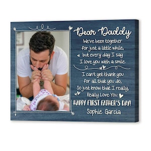 Puede incluir: Placa de madera azul con una foto de un padre y un beb&eacute;, enmarcada con una l&iacute;nea punteada blanca. El texto dice "&iexcl;Feliz D&iacute;a del Padre!" y un mensaje de amor.