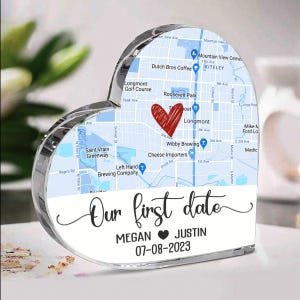 May include: A heart-shaped acrylic keepsake featuring a map with a red heart marking a location. The text "Our first date" is displayed, along with names and a date. A unique personalized gift.