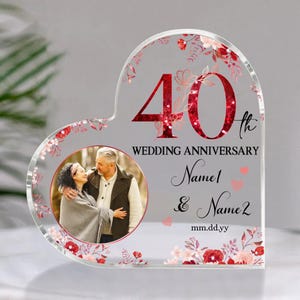 May include: A heart-shaped acrylic anniversary keepsake. The design features a photo of a couple, the number "40" in red, and the words "Wedding Anniversary." Includes space for names and a date, with floral accents.