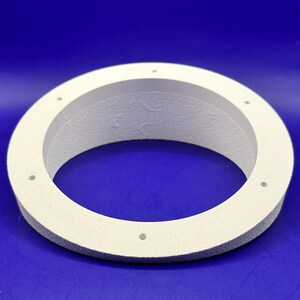 Peut inclure: Un objet circulaire blanc avec une surface texturée et plusieurs petits trous espacés. L'objet est placé sur un fond bleu uni, créant un contraste qui met en valeur sa forme et sa texture. Le design est simple et fonctionnel.