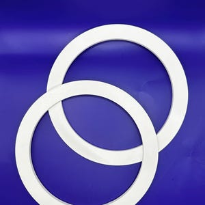 Op de afbeelding: Twee witte, cirkelvormige objecten met een dik, afgerond profiel tegen een diepblauwe achtergrond. De objecten overlappen elkaar licht, waardoor een gelaagd effect ontstaat. Het strakke, minimalistische ontwerp suggereert een focus op vorm.