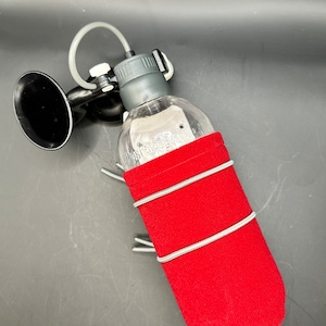 May include: A clear water bottle with a red fabric sleeve and a black horn-shaped component. The bottle has a grey cap and a flexible tube. The red sleeve is secured with silver elastic bands. The horn is black.