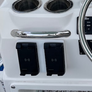 May include: A white boat console with two cup holders, a stainless steel grab bar, and two black wireless charging pads. The console also features a Garmin display and control buttons.