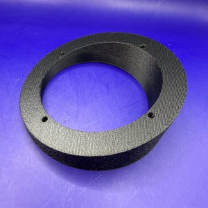 May include: A black, circular, 3D-printed adapter ring with a textured exterior surface. The object features a wide, angled flange and three evenly spaced mounting holes along the flat top surface, designed for secure attachment.