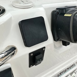 May include: A boat dashboard featuring a black square pad, a white circular control panel with buttons, and a black switch labelled "JACKPLATE". The dashboard is white with chrome detailing. The image shows various boat controls.