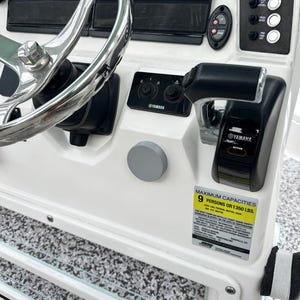 May include: A boat dashboard with a chrome steering wheel, Garmin displays, and Yamaha controls. The dashboard is white with black accents and includes a sticker indicating maximum capacity.