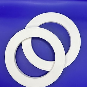May include: Two white, circular objects with a raised, textured surface are positioned on a blue background. The objects are similar in size and shape, resembling rings or hoops. The lighting highlights the texture and form of the objects.
