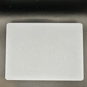 May include: A rectangular, light gray, textured surface. The object has rounded corners and a slightly rough appearance. The background is a dark gray color.