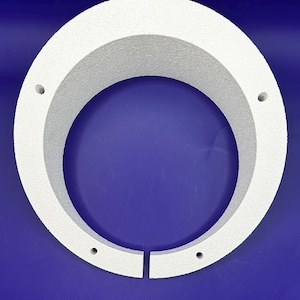Peut inclure: Un objet circulaire blanc avec une surface texturée et une ouverture centrale. L'objet présente une fente en bas et plusieurs petits trous. Le fond est bleu uni.