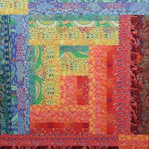 May include: A colorful quilt with a log cabin pattern. The quilt is made of various fabrics with different patterns and colors, including red, orange, yellow, green, blue, and purple.