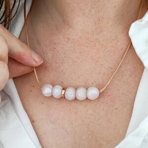 May include: A delicate necklace with a rose gold chain and five white pearl-like beads.