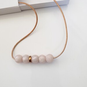 Pink pearl silicone necklace of five small beads seperated with a rose gold spacer bead, necklace placed in giftbox.