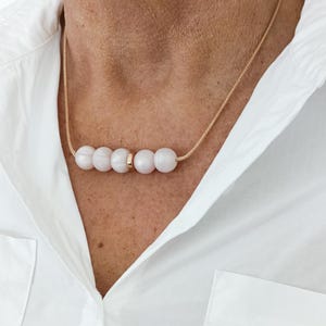 A simple necklace with a rose gold cord and five round, light pink pearl beads. The beads are separated by a gold spacer bead.