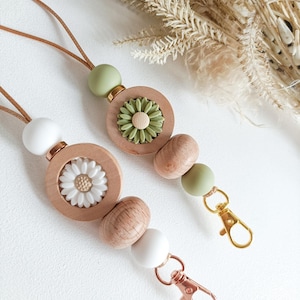 May include: A wooden beaded lanyard with green and white beads, two flower charms, and gold and rose gold lobster clasps.