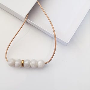 white pearl silicone necklace of five small beads separated with a rose gold spacer bead, necklace placed in giftbox.