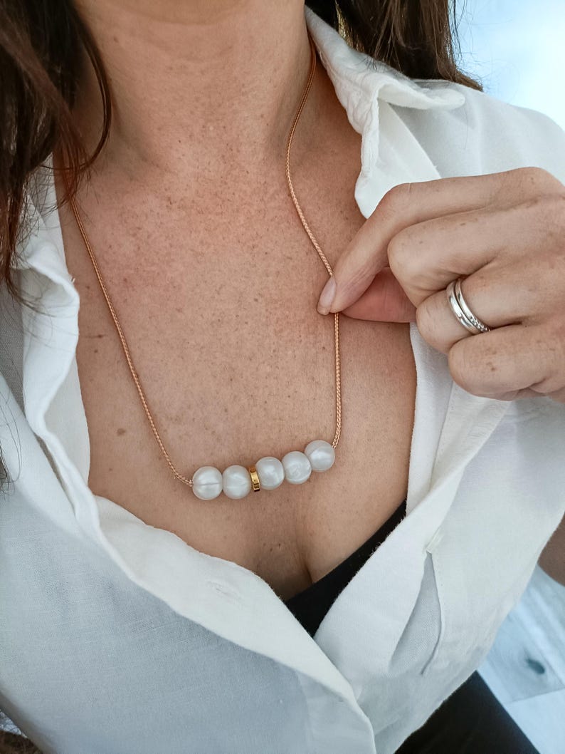 A gold cord chain necklace with a row of five white silicone pearls and a gold accent piece.