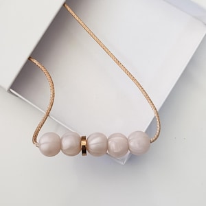 Pink pearl silicone necklace of five small beads separated with a rose gold spacer bead, necklace placed in giftbox.