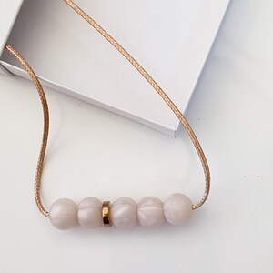 Pink pearl silicone necklace of five small beads separated with a rose gold spacer bead, necklace placed in giftbox.