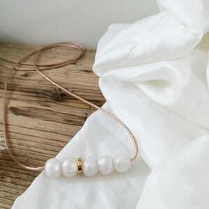 A simple silicone necklace with a gold accent and five white silicone pearls. The necklace is on a light brown wooden surface.