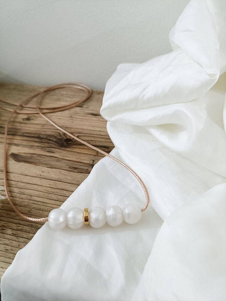 A simple silicone necklace with a gold accent and five white silicone pearls. The necklace is on a light brown wooden surface.