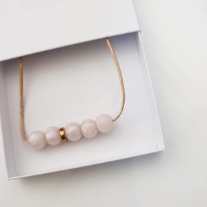 Pink pearl silicone necklace of five small beads separated with a rose gold spacer bead, necklace placed in giftbox.