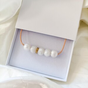 A white silicone pearl necklace with a gold accent piece in a white gift box.