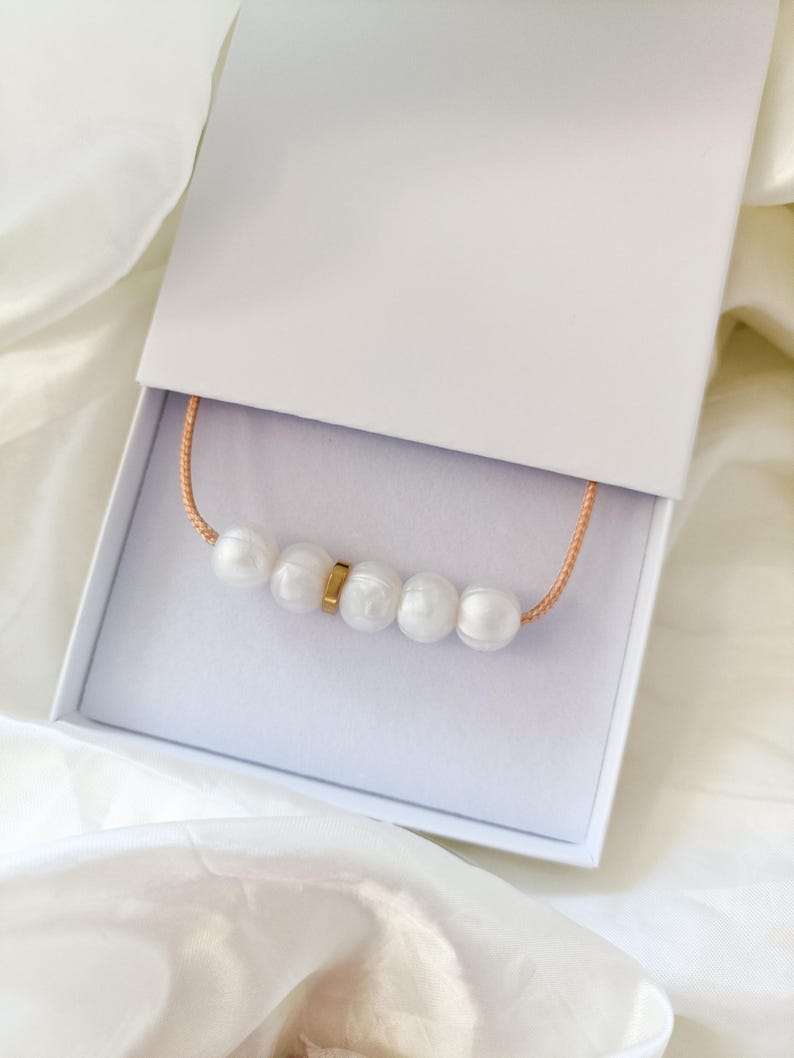 A white silicone pearl necklace with a gold accent piece in a white gift box.