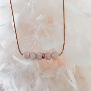 A delicate silicone necklace with a rose gold cord and five pink beads. The beads are arranged in a row with a gold spacer between them.