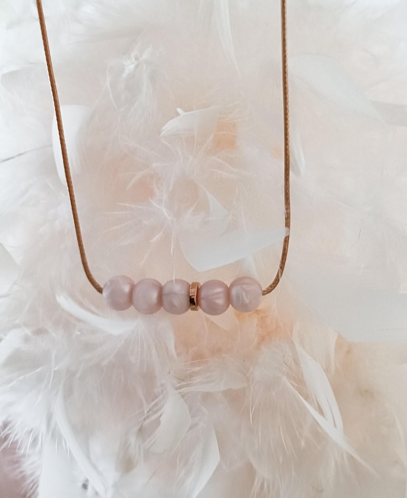 A delicate silicone necklace with a rose gold cord and five pink beads. The beads are arranged in a row with a gold spacer between them.