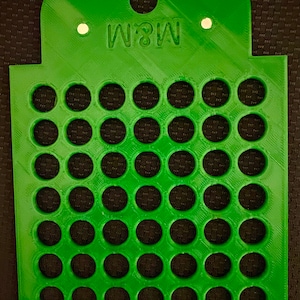 Może przedstawiać: Zielony plastikowy organizer do przechowywania z siatką 42 okrągłych otworów. Organizer ma uchwyt na górze, a na przodzie nadrukowany jest tekst "M&M".