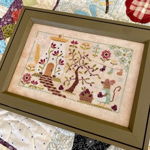 Peut inclure: Image d'une broderie encadrée représentant une scène fantaisiste avec une maison, un arbre et une souris. L'œuvre est dans un cadre vert et présente un design détaillé avec des éléments floraux et fruités. La palette de couleurs comprend des nuances de rose, de vert et de marron.