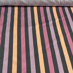 Könnte beinhalten: Gestreifter Stoff in den Farben Pfirsich, Rosa, Lila und Schwarz. Der Stoff ist in der Mitte gefaltet und zeigt das Muster auf beiden Seiten.