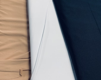 May include: A close-up of three rolls of fabric in different colors. The colors are tan, white, and navy blue. The fabric is tightly rolled and appears to be a smooth material. The image is well-lit, showing the texture and color variations.
