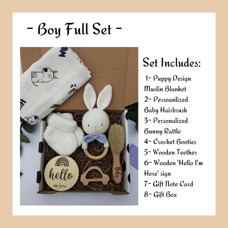 May include: A gift box set for a baby, containing a white muslin blanket with a puppy design, a white crocheted bunny rattle, a wooden teether, a wooden sign that says "hello I'm here", a crocheted booties, a baby hairbrush, and a gift note card. The box is decorated with black polka dots.
