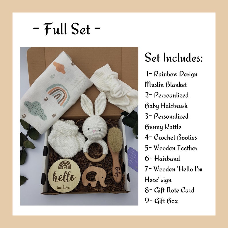 May include: A gift box filled with baby items, including a rainbow muslin blanket, a crocheted bunny rattle, a wooden teether, a hairband, a wooden sign that says "hello I'm here", a crochet bootie, a baby hairbrush, and a gift note card. The box is decorated with black and white polka dots.