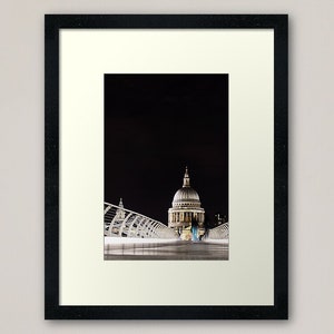 Può includere: Una vista notturna della Cattedrale di San Paolo a Londra, illuminata contro un cielo scuro. La cattedrale è vista da un ponte con una struttura moderna in metallo bianco.