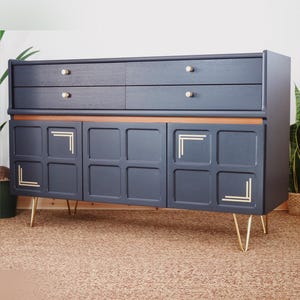 Peut inclure: Un buffet vintage noir avec des accents dorés et trois portes. Le buffet a quatre tiroirs et repose sur des pieds en épingle à cheveux dorés.