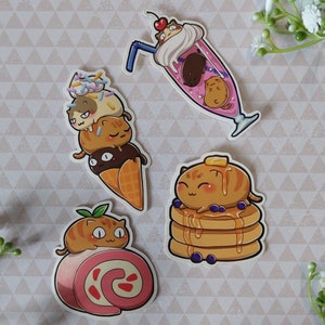 May include: Four colourful stickers featuring cute cartoon cats enjoying different desserts. The first sticker shows a cat with a cone of ice cream with a cat face on top. The second sticker shows a cat enjoying a milkshake with a cherry on top. The third sticker shows a cat enjoying a stack of pancakes. The fourth sticker shows a cat enjoying a strawberry roll.