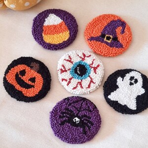 May include: Six handmade Halloween-themed felt ornaments. The ornaments are round and feature various designs, including a candy corn, a witch's hat, an eyeball, a pumpkin, a ghost, and a spider.