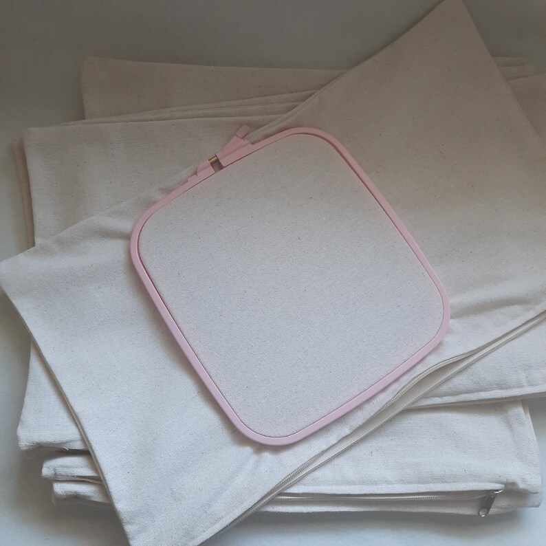 May include: A stack of white fabric squares with a pink embroidery hoop on top. The fabric squares have zippers on the sides.