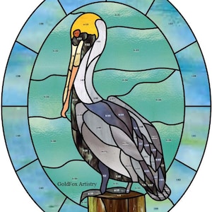 May include: Stained glass artwork depicting a pelican on a wooden post. The bird is rendered in shades of grey, white, yellow, and orange, set against a teal and blue background within an oval frame. The artwork is signed "GoldFox Artistry".