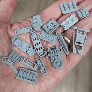 Könnte beinhalten: Eine Sammlung kleiner, unbemalter hellgrauer Harzkomponenten mit komplexen mechanischen Details, geometrischen Formen und strukturierten Oberflächen. Diese Miniaturteile umfassen verschiedene rechteckige, kreisförmige und geschlitzte Formen.