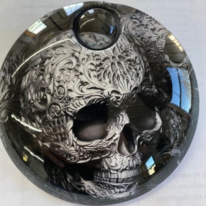 May include: A black and white skull with intricate floral designs, printed on a round, black gas cap.