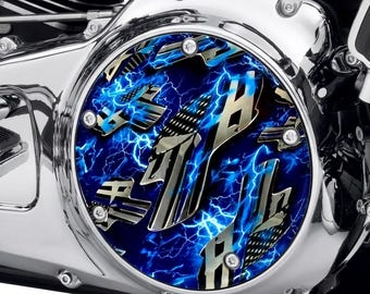 May include: A circular motorcycle derby cover featuring a vibrant blue lightning pattern background with metallic, silver-toned American flag graphics overlaid. The cover is secured with five silver bolts to a polished chrome engine housing.