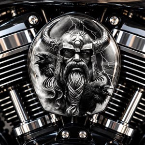 May include: A circular motorcycle air cleaner cover featuring a detailed black and white illustration of a bearded warrior wearing a horned helmet with two ravens and lightning bolts in the background, mounted on a metallic engine block.