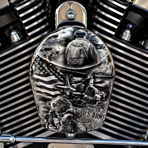 May include: A motorcycle air cleaner cover featuring a black and white airbrushed graphic of a soldier with a backpack, a helicopter, a waving American flag, and paratroopers. The text U.S. ARMY is printed in black on the lower right side.